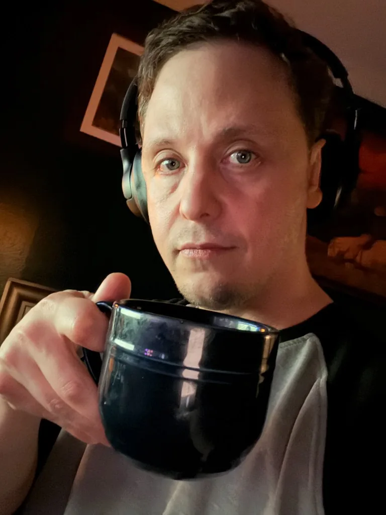 A CI Web Group teammate at a home workstation wearing headphones and holding a large dark mug