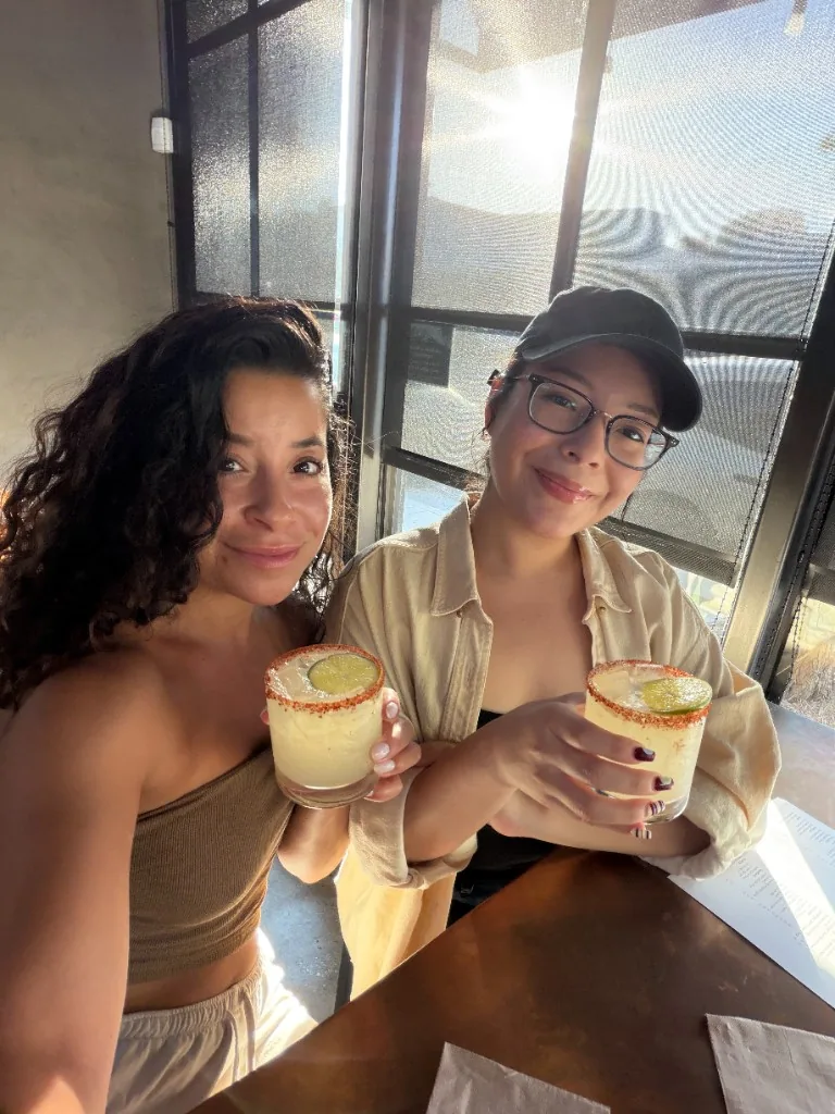 Two CI Web Group teammates at a sunlit table holding chili-rimmed margaritas garnished with lime