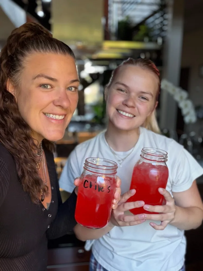 Two CI Web Group teammates smiling, each holding a mason jar of a bright red drink