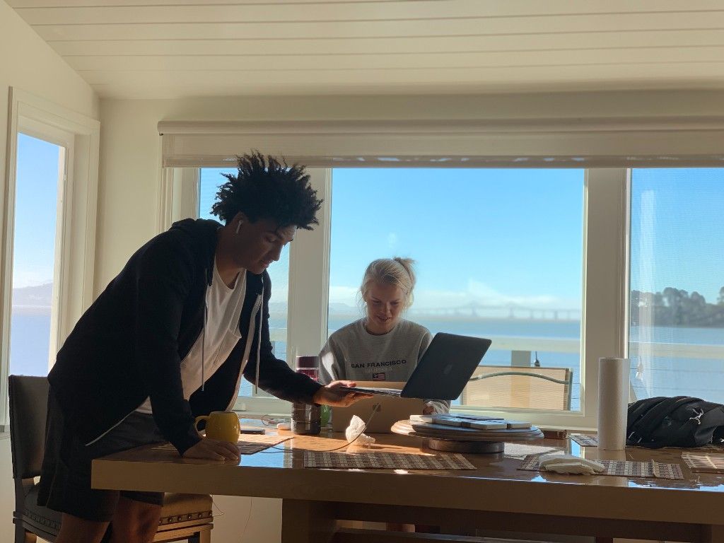 Two CI Web Group team members working at a table by a window with a bay view