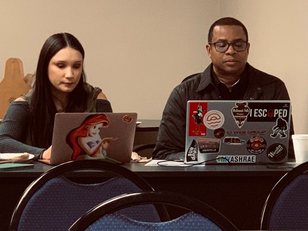Two CI Web Group team members working on sticker-covered laptops at a conference table