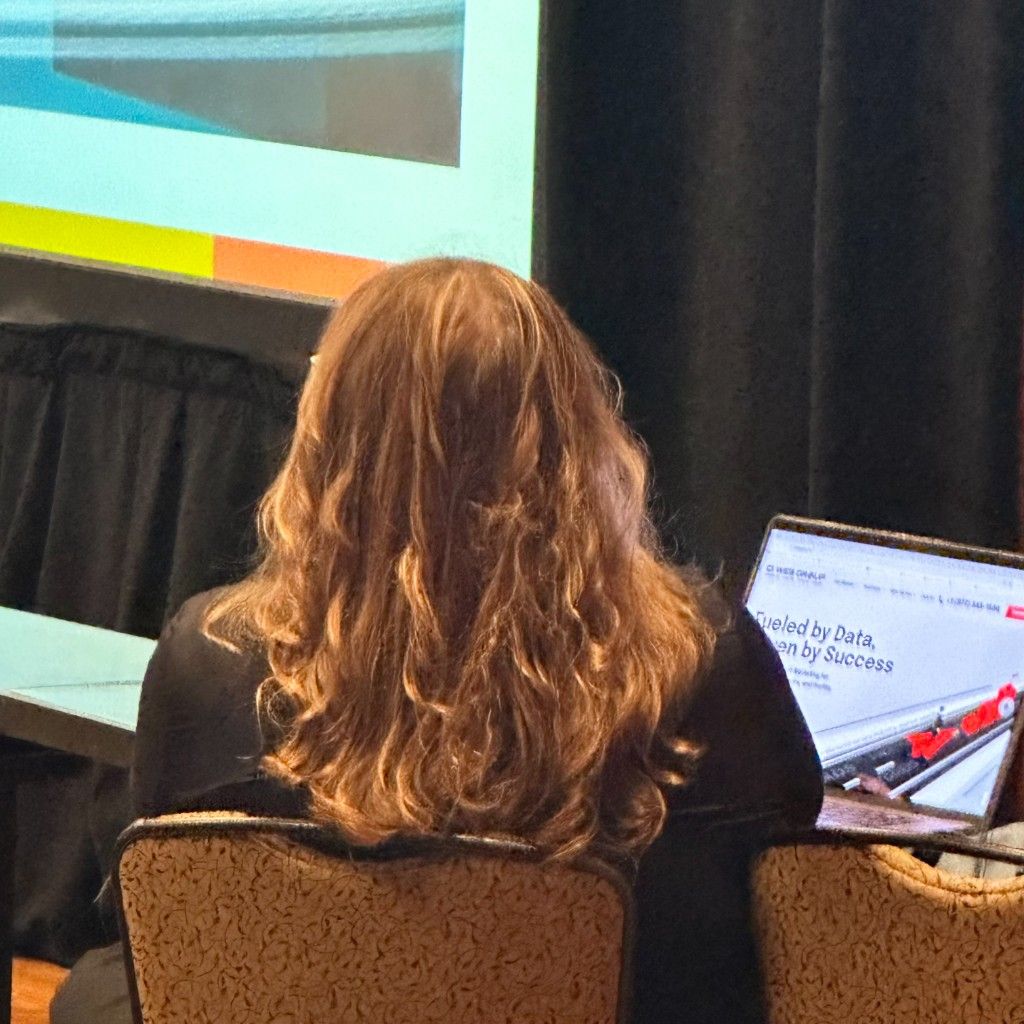 A CI Web Group team member working at an event beside a 'Fueled by Data' screen