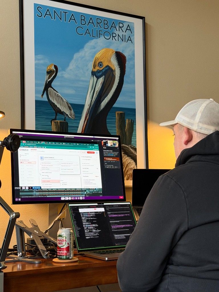A CI Web Group team member at a home desk with a Santa Barbara poster and multiple screens