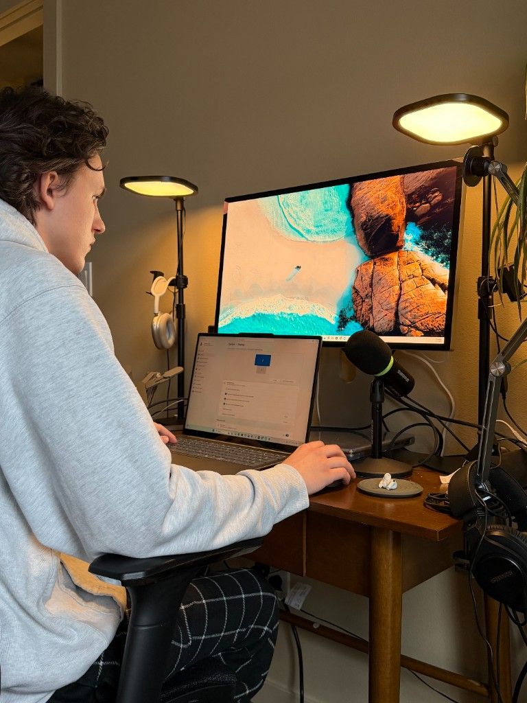 A CI Web Group team member at a dual-monitor home studio desk with a microphone