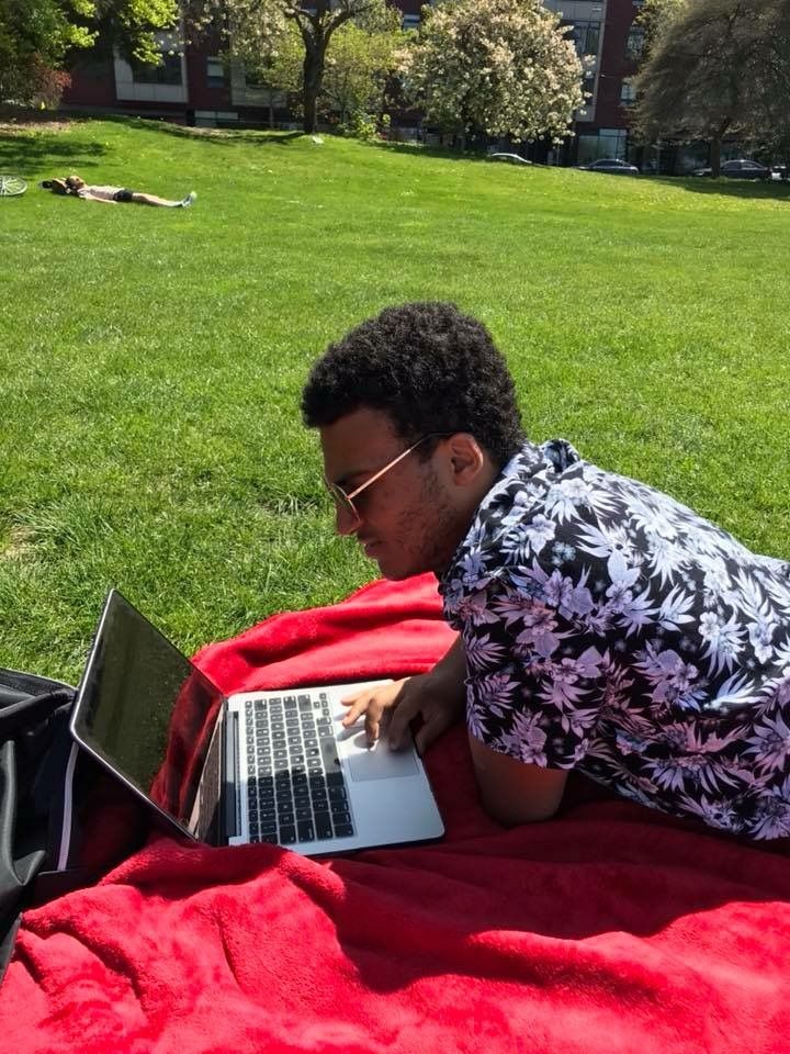 A CI Web Group team member working on a laptop on a blanket in a park