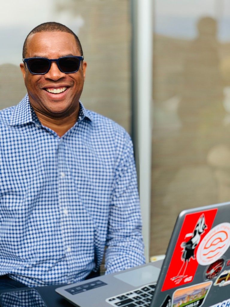 A smiling CI Web Group team member working on a laptop outdoors in sunglasses