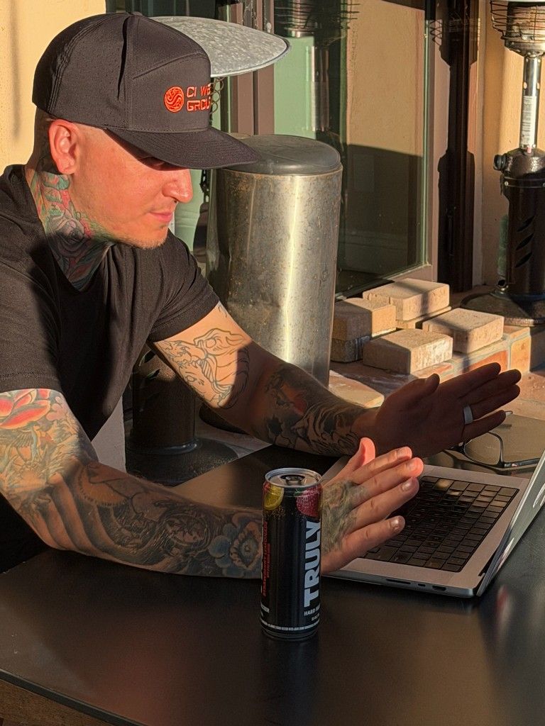 A CI Web Group team member in a branded cap working on a laptop on a patio