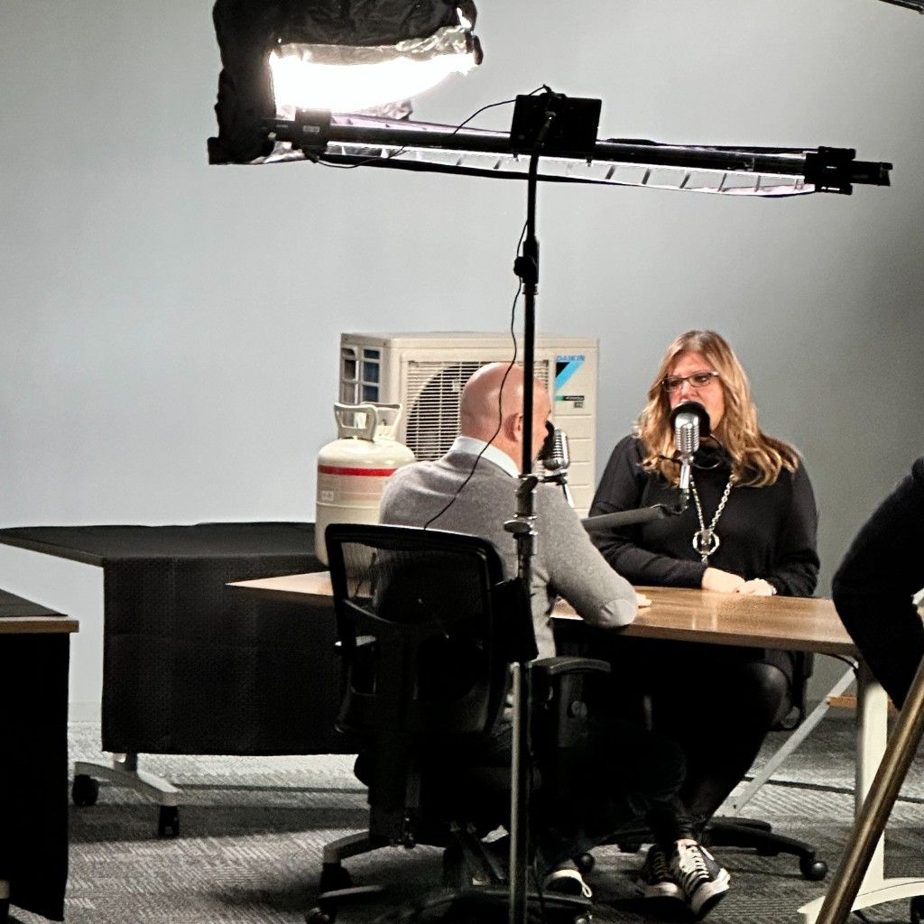 Two people recording at microphones under a studio light in a production room