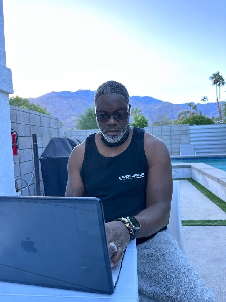 A CI Web Group team member in branded apparel working on a laptop poolside with mountains behind
