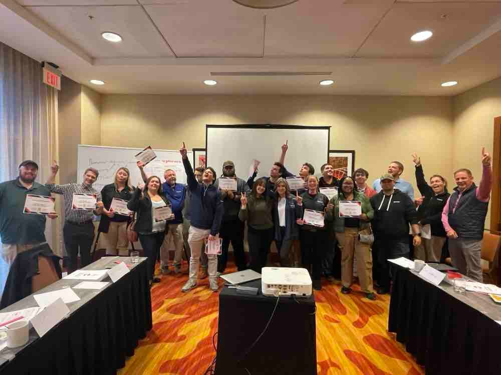 Contractors celebrating with manufacturer roadshow signs at a CI Web Group training event