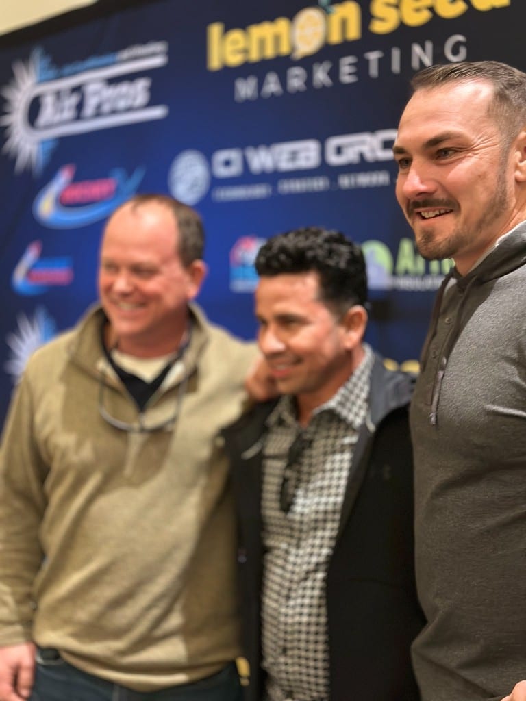 Three trades professionals in front of a sponsor wall at an industry event