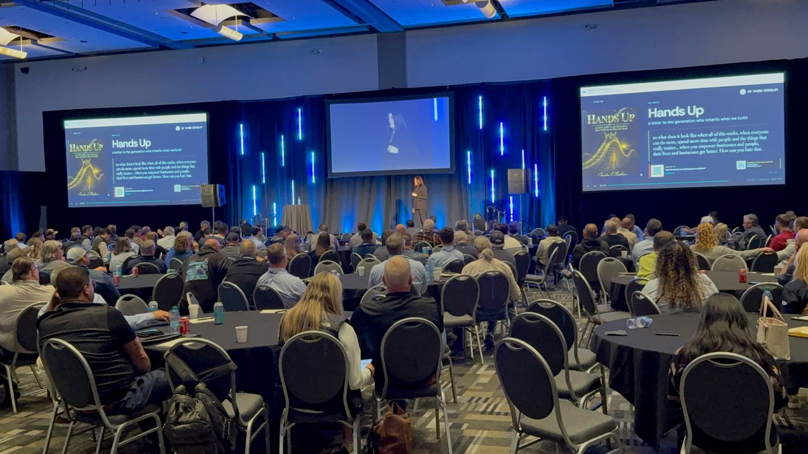 A packed ballroom watching Jennifer Bagley's Hands Up keynote on three screens