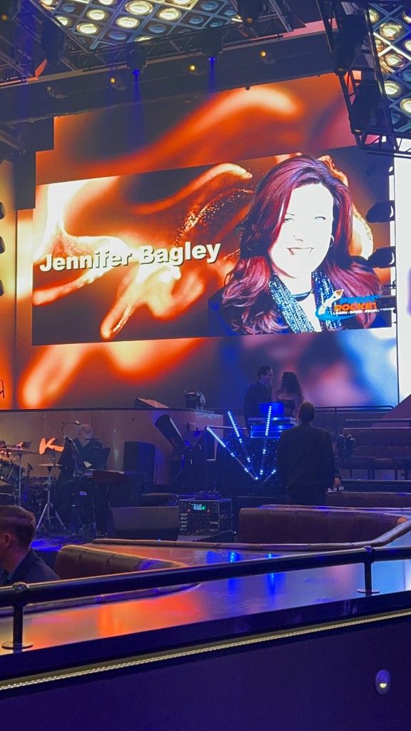 A large event screen featuring CI Web Group CEO Jennifer Bagley at a trades conference